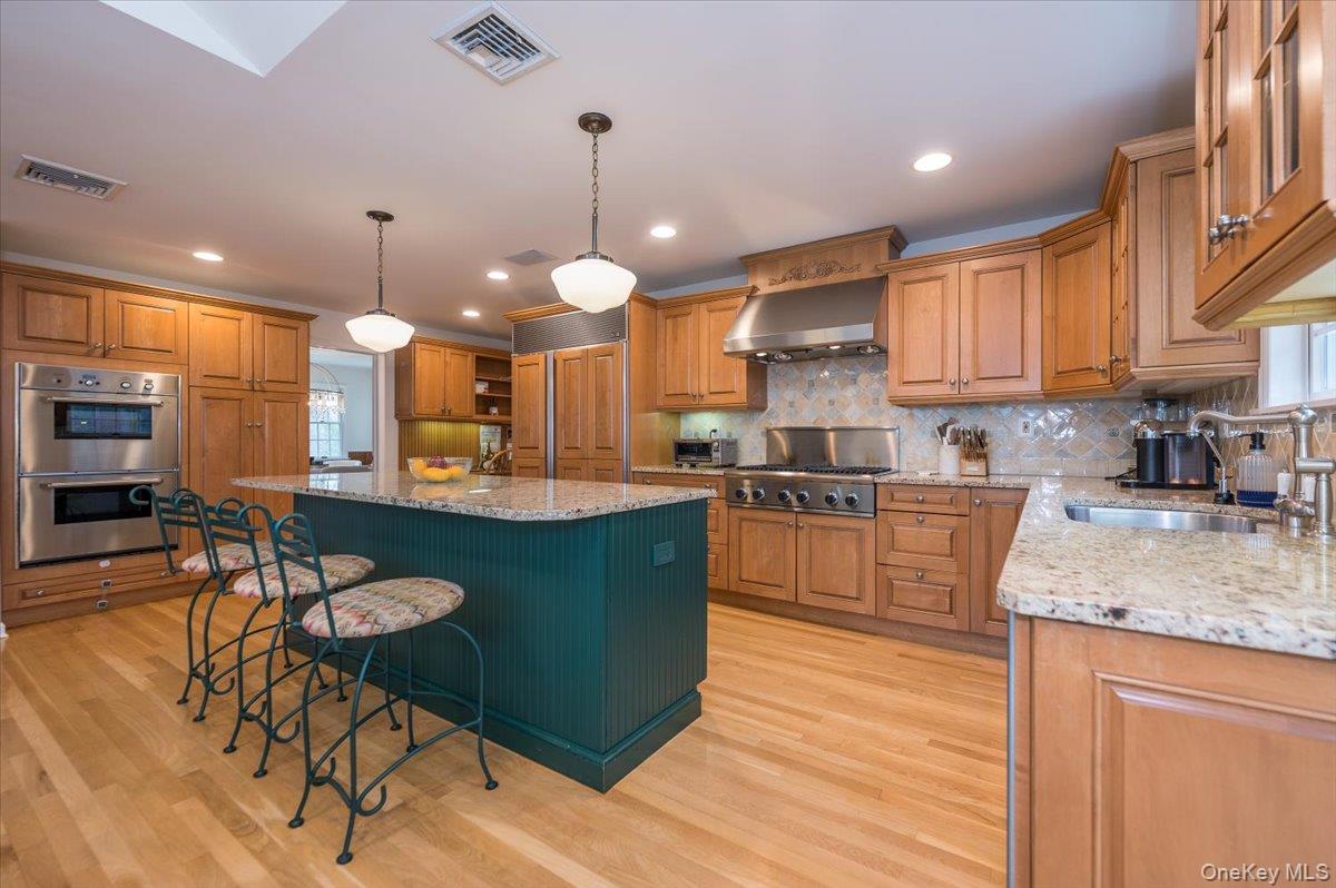 4 Springwood Path Syosset, NY 11791 - Photo 12 of 47 The kitchen features hardwood floors, a large island with a granite countertop, and light wood cabinetry with stainless steel appliances