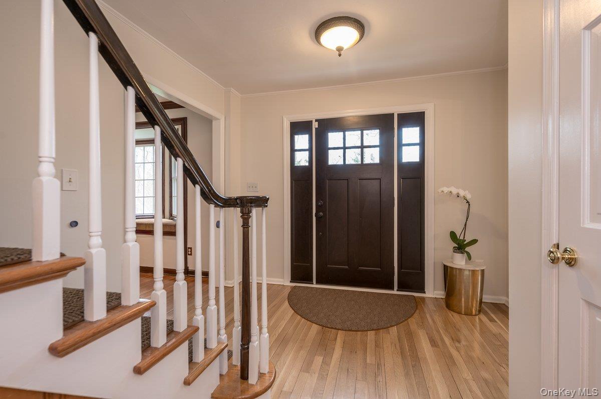 4 Springwood Path Syosset, NY 11791 - Photo 20 of 47 Welcoming entryway featuring light hardwood floors, a dark wood front door with glass panes, and a staircase with white balusters and wood handrails