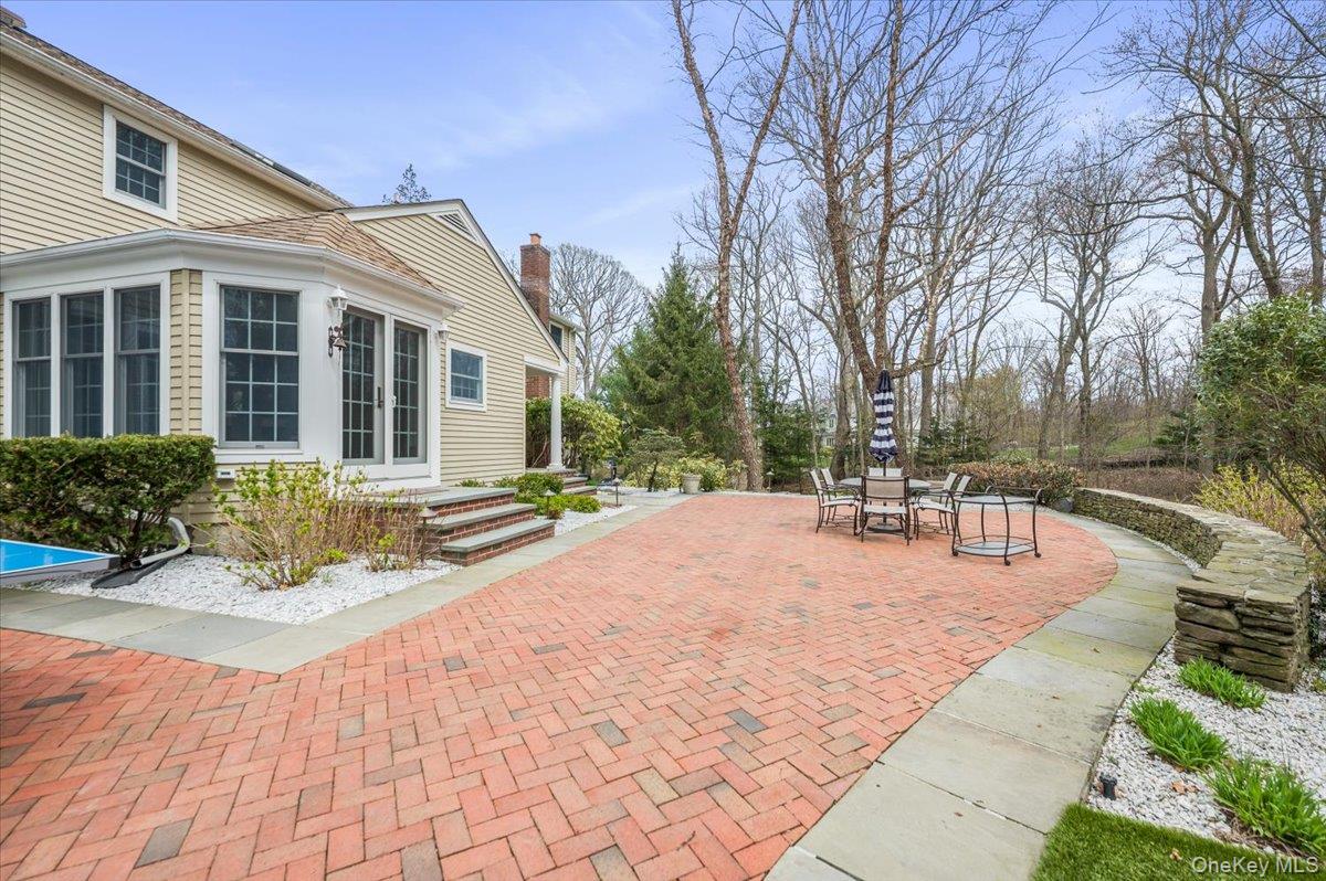 4 Springwood Path Syosset, NY 11791 - Photo 38 of 47 The property features a spacious brick patio, a stone retaining wall, and a well-maintained lawn area