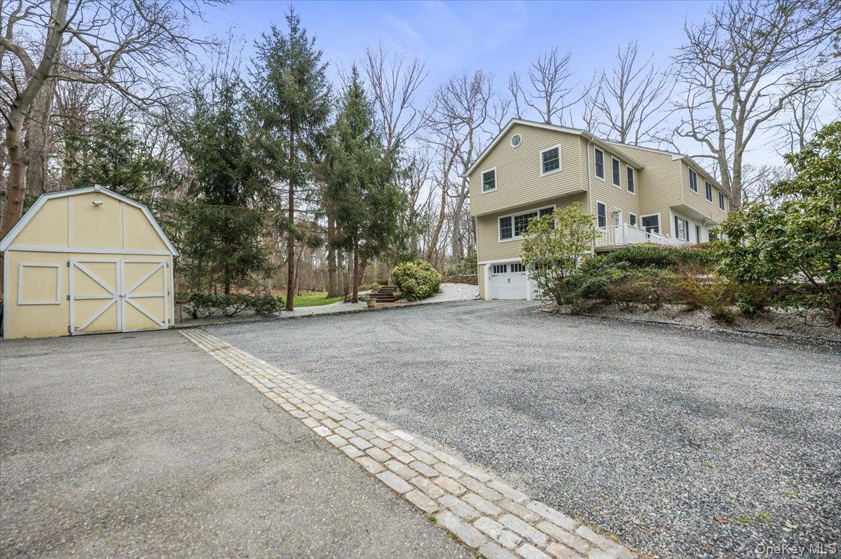 4 Springwood Path Syosset, NY 11791 - Photo 46 of 47 Large gravel driveway with a cobblestone accent, a detached barn-style shed, and attached two-car garage.
