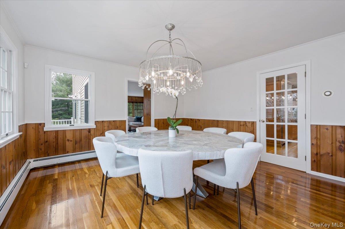 4 Springwood Path Syosset, NY 11791 - Photo 9 of 47 Dining area featuring hardwood floors, wood paneling, and a decorative chandelier. French door leading to kitchen.