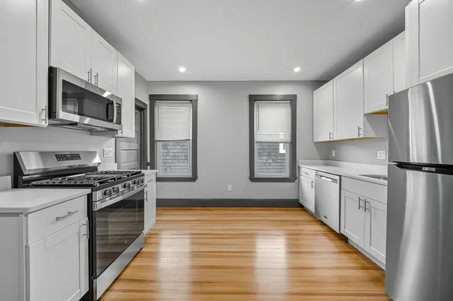 a kitchen with stainless steel appliances granite countertop a stove top oven a sink dishwasher a refrigerator and white cabinets with wooden floor