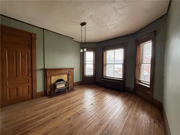 a view of an empty room with wooden floor fireplace and a window