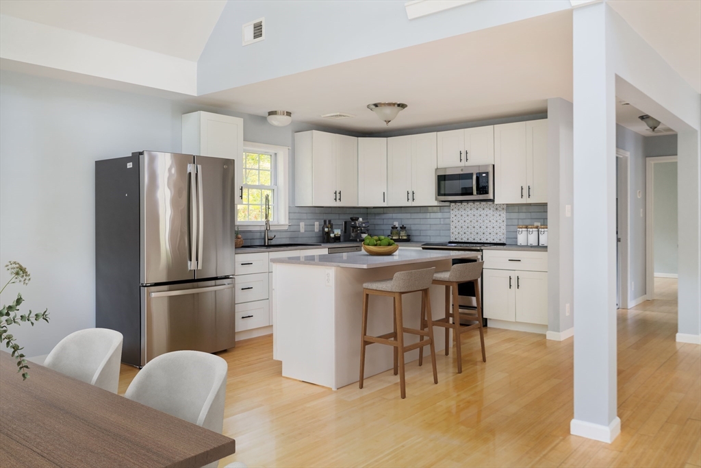 267 Carlisle Road Bedford, MA 01730 - Photo 4 of 32 a kitchen with stainless steel appliances granite countertop a refrigerator a stove a sink a dining table and chairs with wooden floor