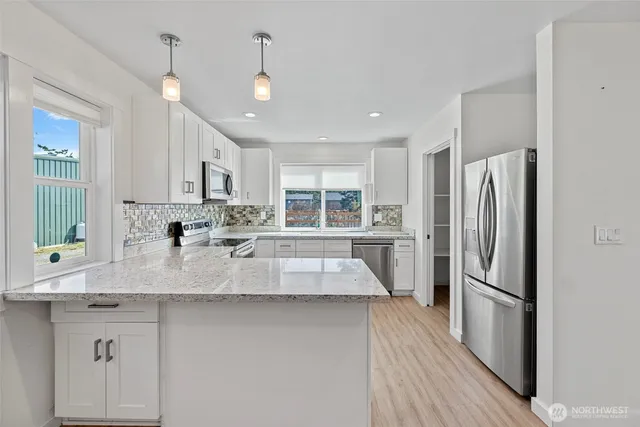 a kitchen with kitchen island granite countertop white cabinets a sink a window and stainless steel appliances