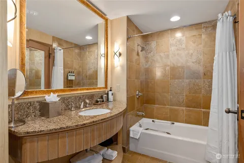 a bathroom with a granite countertop sink a mirror a bathtub and shower