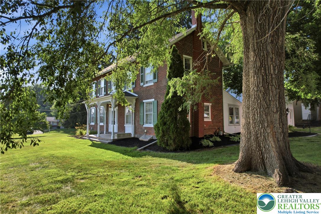4682 Steuben Road Bethlehem, PA 18020 - Photo 76 of 79 A classic brick dwelling with light green shutters stands tall, surrounded by a verdant lawn and mature shade trees.