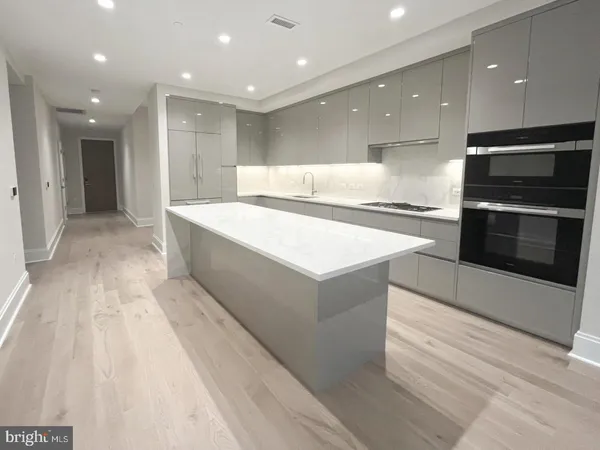 a large kitchen with stainless steel appliances kitchen island a large counter top and a stove top oven with wooden floor
