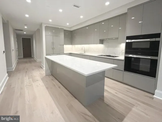 a large kitchen with stainless steel appliances kitchen island a large counter top and a stove top oven with wooden floor