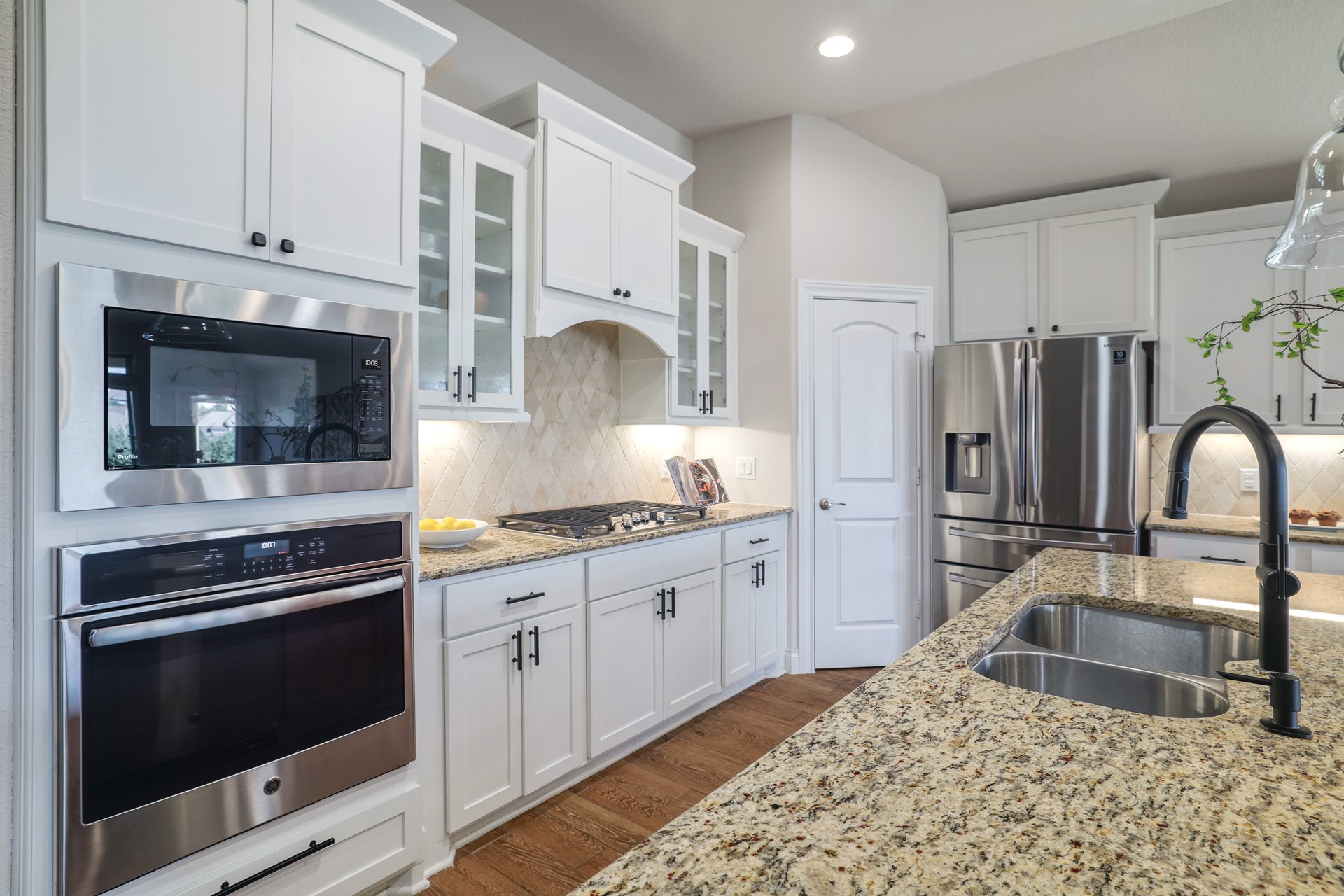 173 Santa Maria Street Georgetown, TX 78628 - Photo 18 of 39 Kitchen featuring stainless steel appliances, light granite countertops, white cabinetry with black hardware, and wood-finish flooring