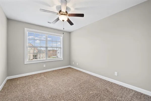 an empty room with a chandelier fan and windows