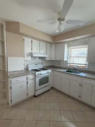 a large white kitchen with granite countertop white cabinets a sink a stove and dishwasher