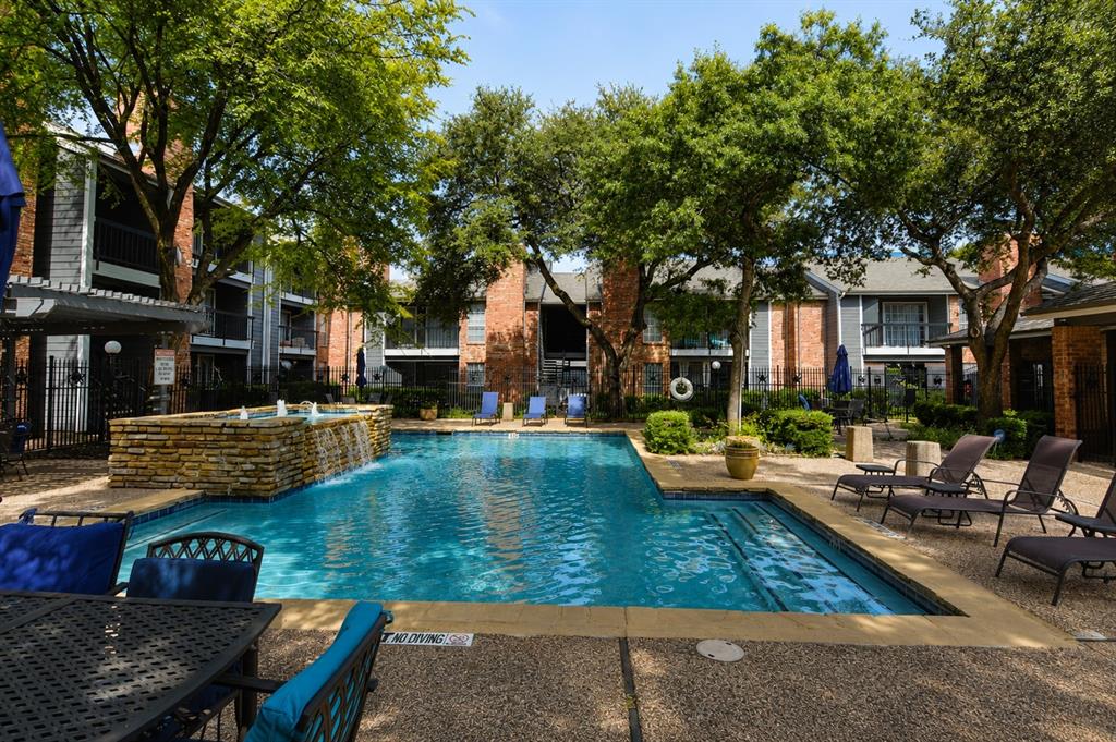 18333 Roehampton Drive, Unit 1036 Dallas, TX 75252 - Photo 9 of 12 Resort-style swimming pool featuring a stone-clad waterfall, surrounding sundeck, and lush mature trees providing shade