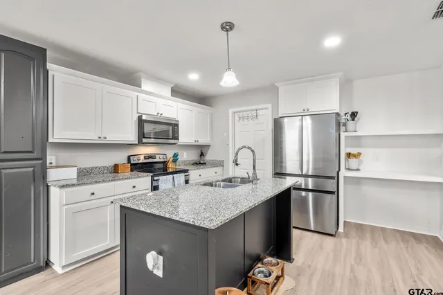 a kitchen with stainless steel appliances granite countertop a refrigerator a sink dishwasher a microwave oven a stove with white cabinets and wooden floor