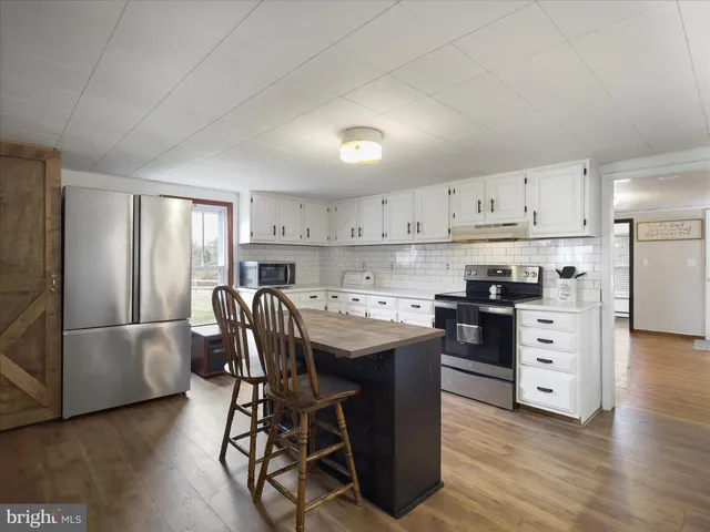 a room with kitchen island granite countertop wooden floors and white stainless steel appliances