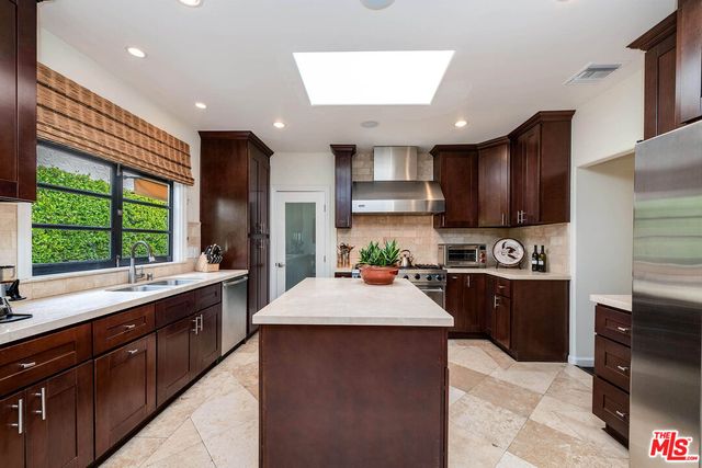 a large kitchen with stainless steel appliances kitchen island granite countertop a sink counter space cabinets and a large window