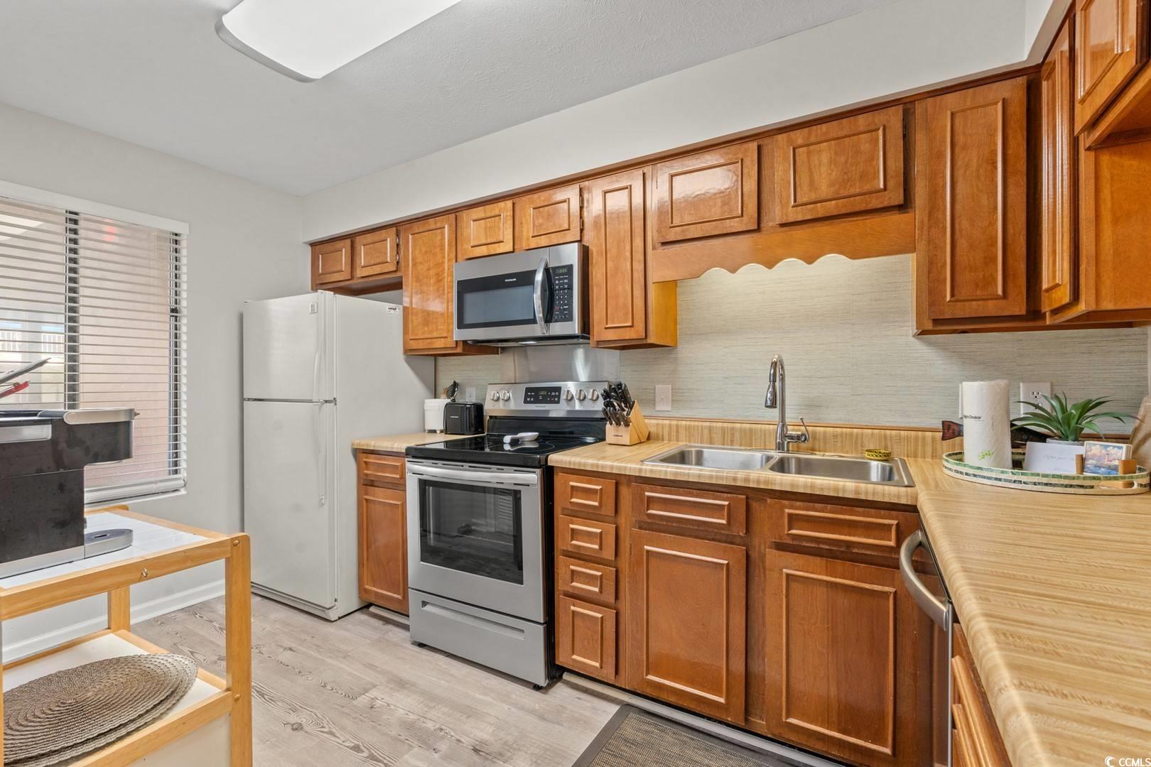 5507 North Ocean Boulevard, Unit 113 Myrtle Beach, SC 29577 - Photo 8 of 28 Kitchen with stainless steel appliances, light countertops, light wood-style flooring, brown cabinetry, and decorative backsplash