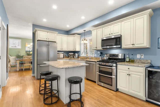 a kitchen with stainless steel appliances granite countertop a stove a sink a refrigerator and white cabinets with wooden floor