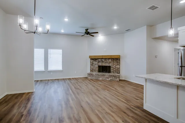 an empty room with wooden floor fireplace and chandelier