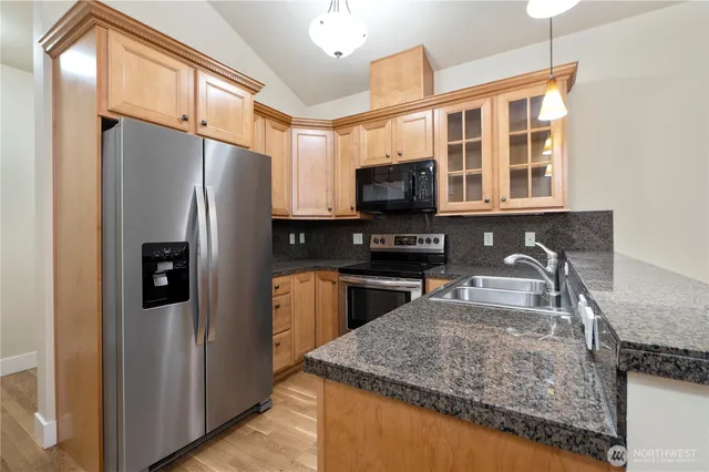a kitchen with stainless steel appliances granite countertop a refrigerator a stove and a sink with wooden floor