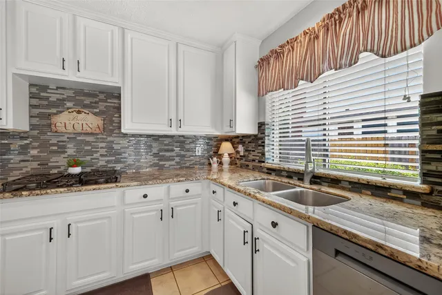 a kitchen with granite countertop a sink a white cabinets and a window
