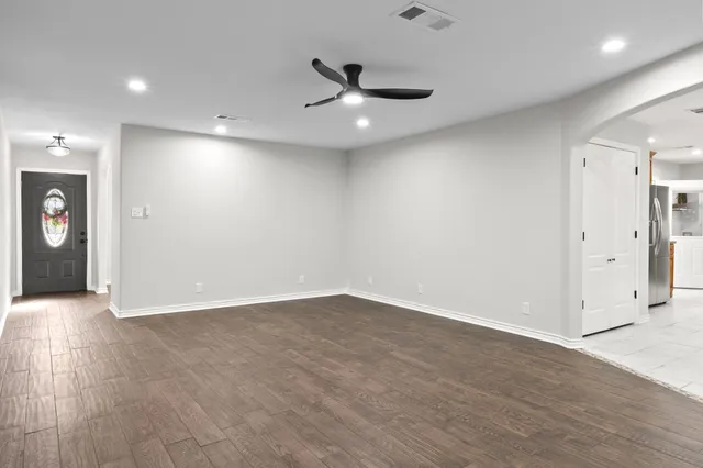 an empty room with wooden floor a ceiling fan and windows