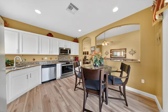 a kitchen with stainless steel appliances granite countertop a stove top oven a sink dishwasher white cabinets and a dining table with wooden floor