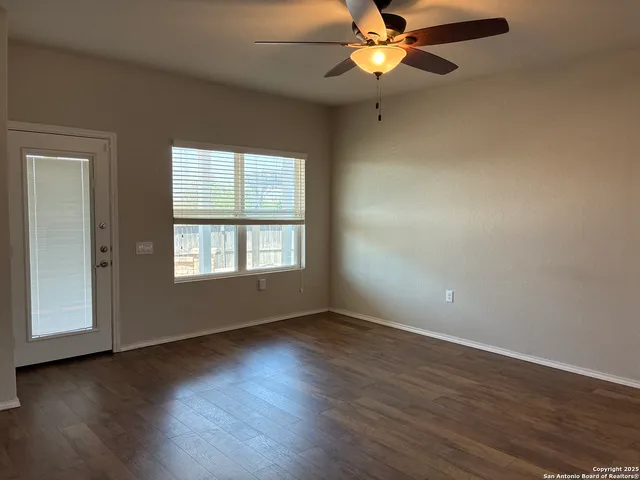an empty room with wooden floor chandelier fan and windows