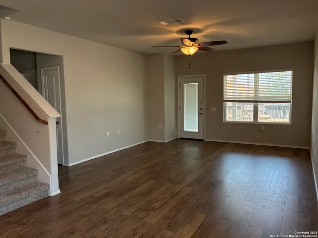 an empty room with wooden floor chandelier fan and windows