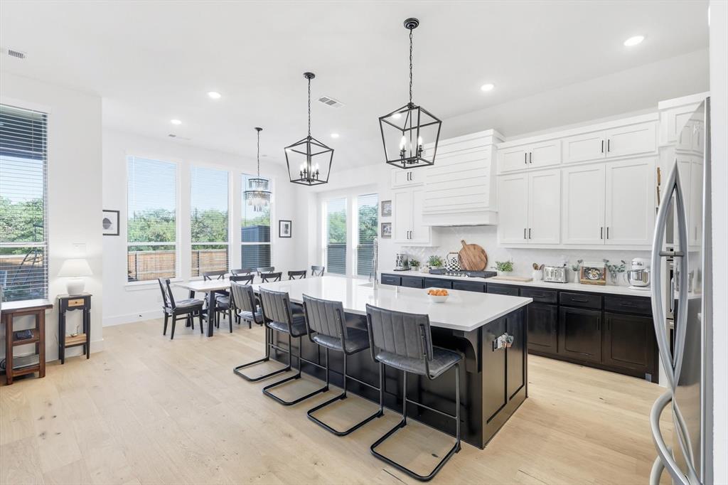 4608 Mount Vista Road Oak Point, TX 75068 - Photo 17 of 39 Open-concept kitchen featuring a large island with countertop seating, light wood-finish flooring, and white upper cabinetry contrasting with dark lower cabinetry