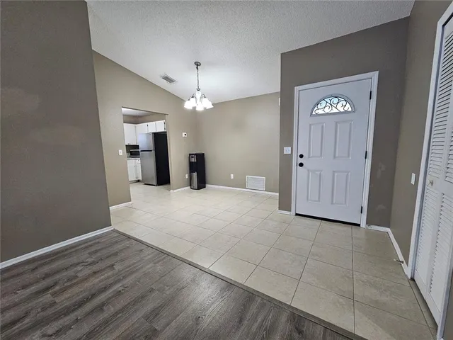 an empty room with kitchen view and a chandelier