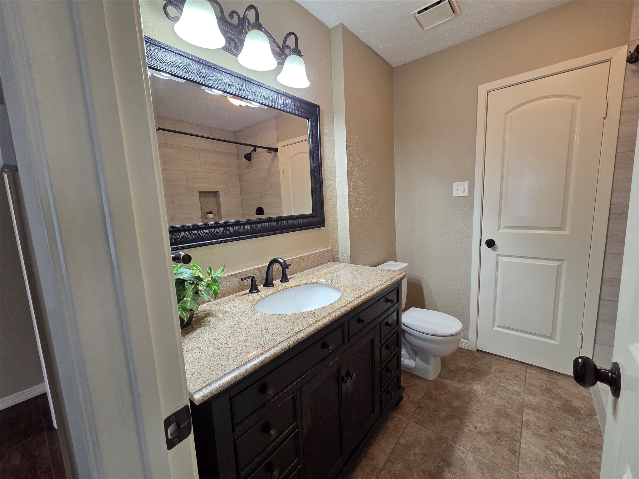4203 Spinks Creek Lane Spring, TX 77388 - Photo 8 of 14 The full bathroom features a modern design with a granite countertop, dark wood vanity, and large framed mirror. It has tile flooring, a well-lit space with three light fixtures, and a walk in shower with neutral tile.