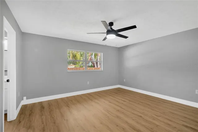 an empty room with wooden floor a ceiling fan and windows