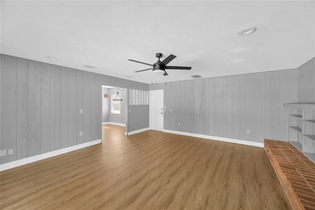 a view of an empty room with wooden floor and a ceiling fan
