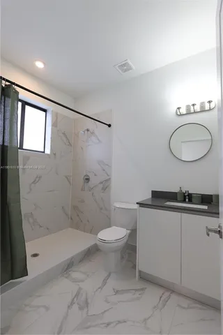 a bathroom with a granite countertop sink a toilet a mirror and shower