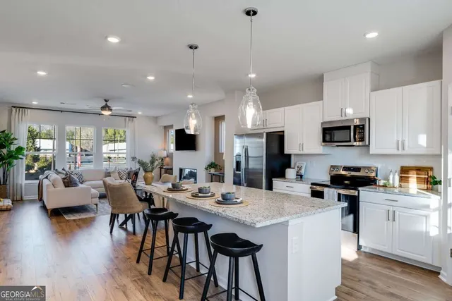 a kitchen with stainless steel appliances kitchen island granite countertop a refrigerator a stove a sink a dining table and chairs with wooden floor