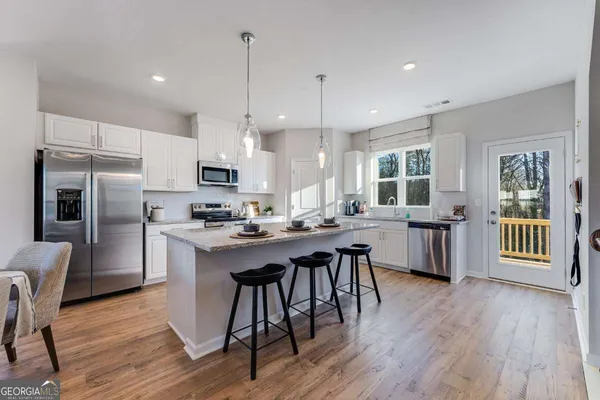 a kitchen with stainless steel appliances granite countertop a refrigerator a stove top oven a sink dishwasher a dining table and chairs with wooden floor