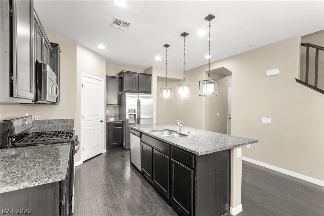 11048 Prairie Grove Road Las Vegas, NV 89179 - Photo 14 of 75 A contemporary kitchen features dark cabinetry, granite counters, stainless steel appliances, and a large island with pendant lighting.