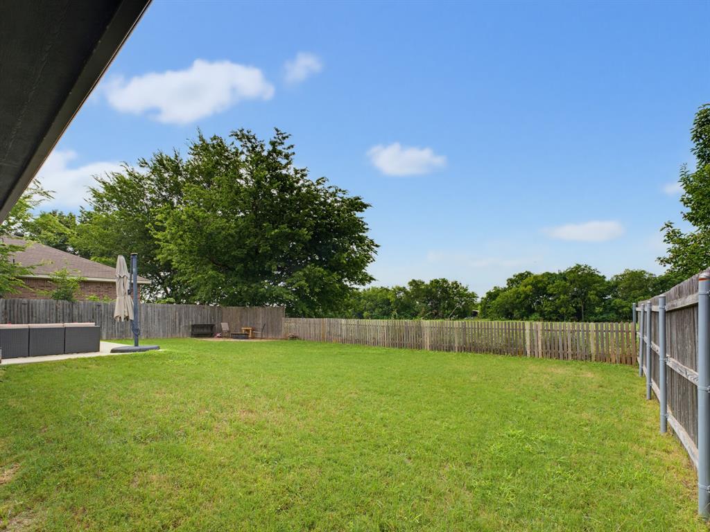 600 Stirling Road Rhome, TX 76078 - Photo 28 of 38 Expansive rear yard featuring a large grass area, a concrete patio, and mature perimeter trees