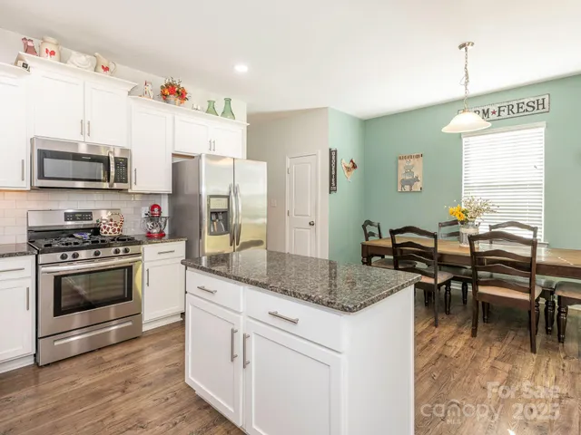 a kitchen with stainless steel appliances granite countertop a stove top oven a sink dishwasher a dining table and chairs with wooden floor