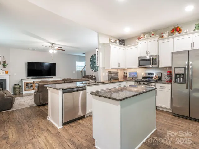 a kitchen with stainless steel appliances granite countertop a stove top oven a sink dishwasher a refrigerator and a dining table with wooden floor