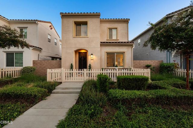 a view of a brick house with a yard plants and large tree
