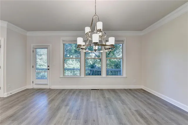 an empty room with wooden floor chandelier and windows
