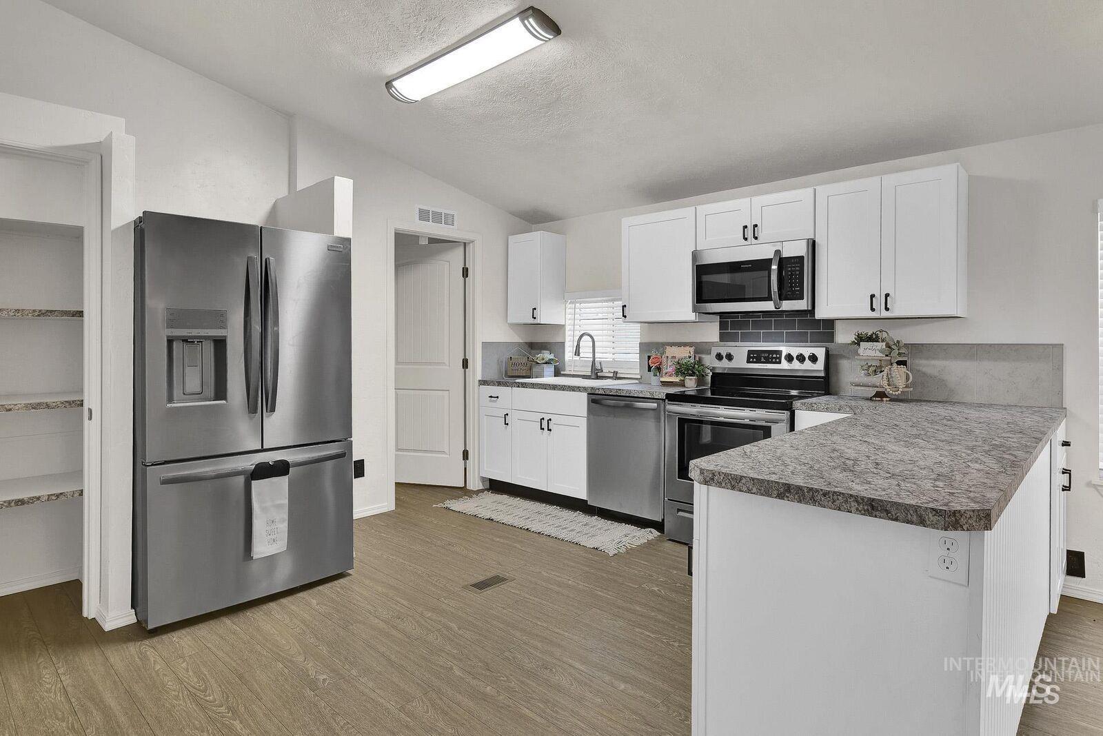 Kitchen featuring stainless steel appliances, white cabinetry, vaulted ceiling, a peninsula, and light wood finished floors