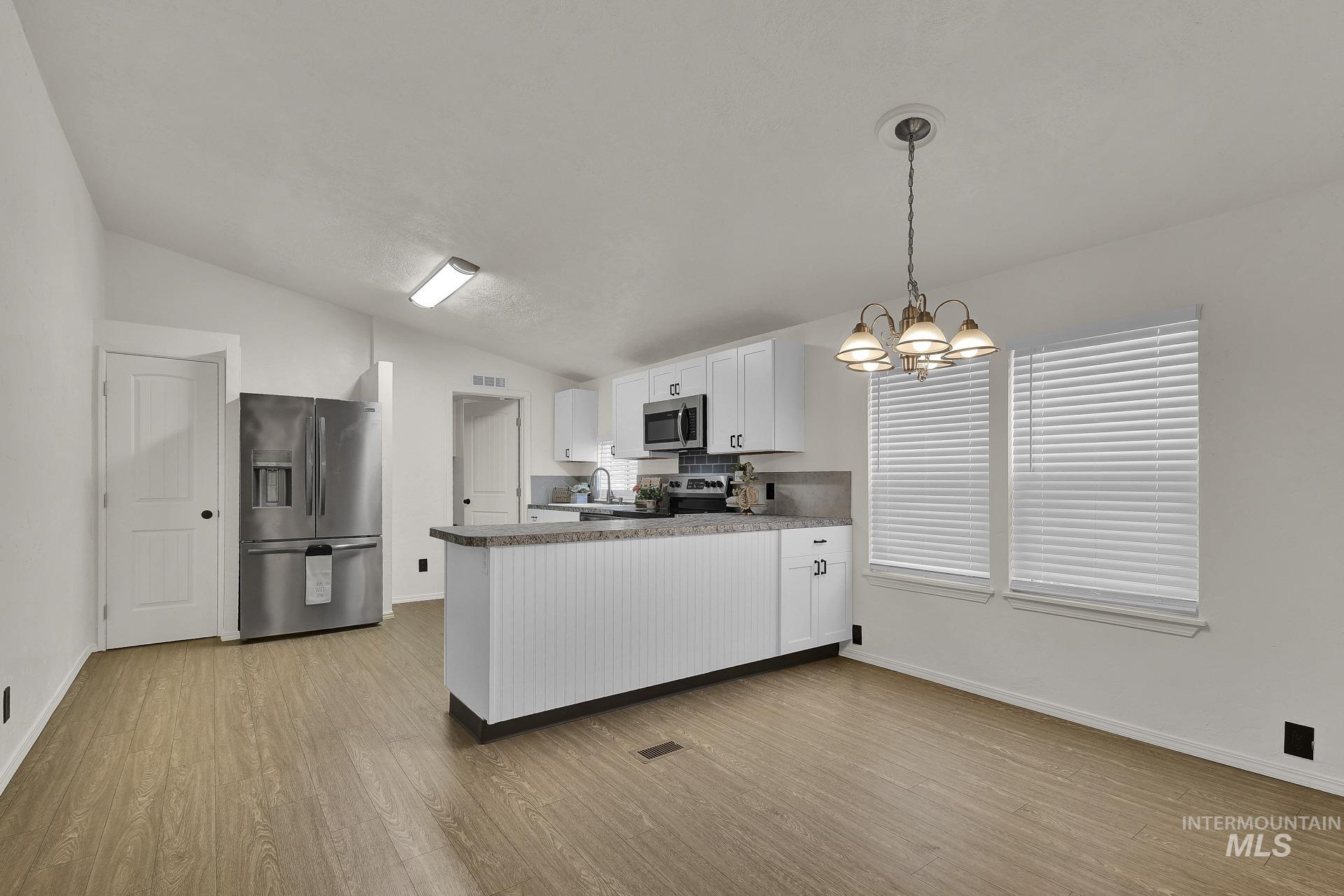 3249 Cherry Lane, Unit 23 Boise, ID 83705 - Photo 7 of 11 Kitchen featuring white cabinets, a peninsula, lofted ceiling, appliances with stainless steel finishes, and decorative light fixtures