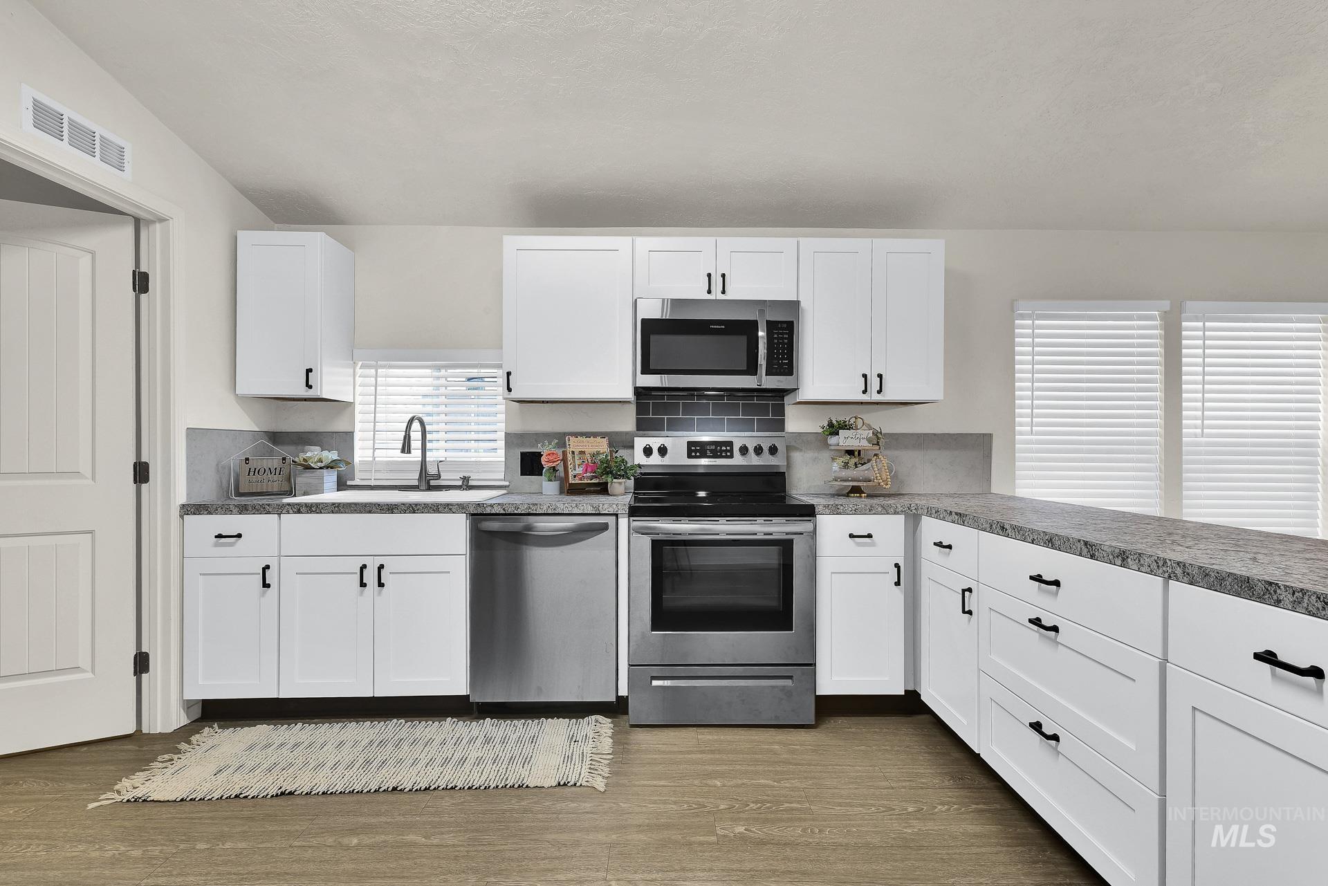 3249 Cherry Lane, Unit 23 Boise, ID 83705 - Photo 8 of 11 Kitchen featuring stainless steel appliances, white cabinetry, dark wood-style flooring, and backsplash