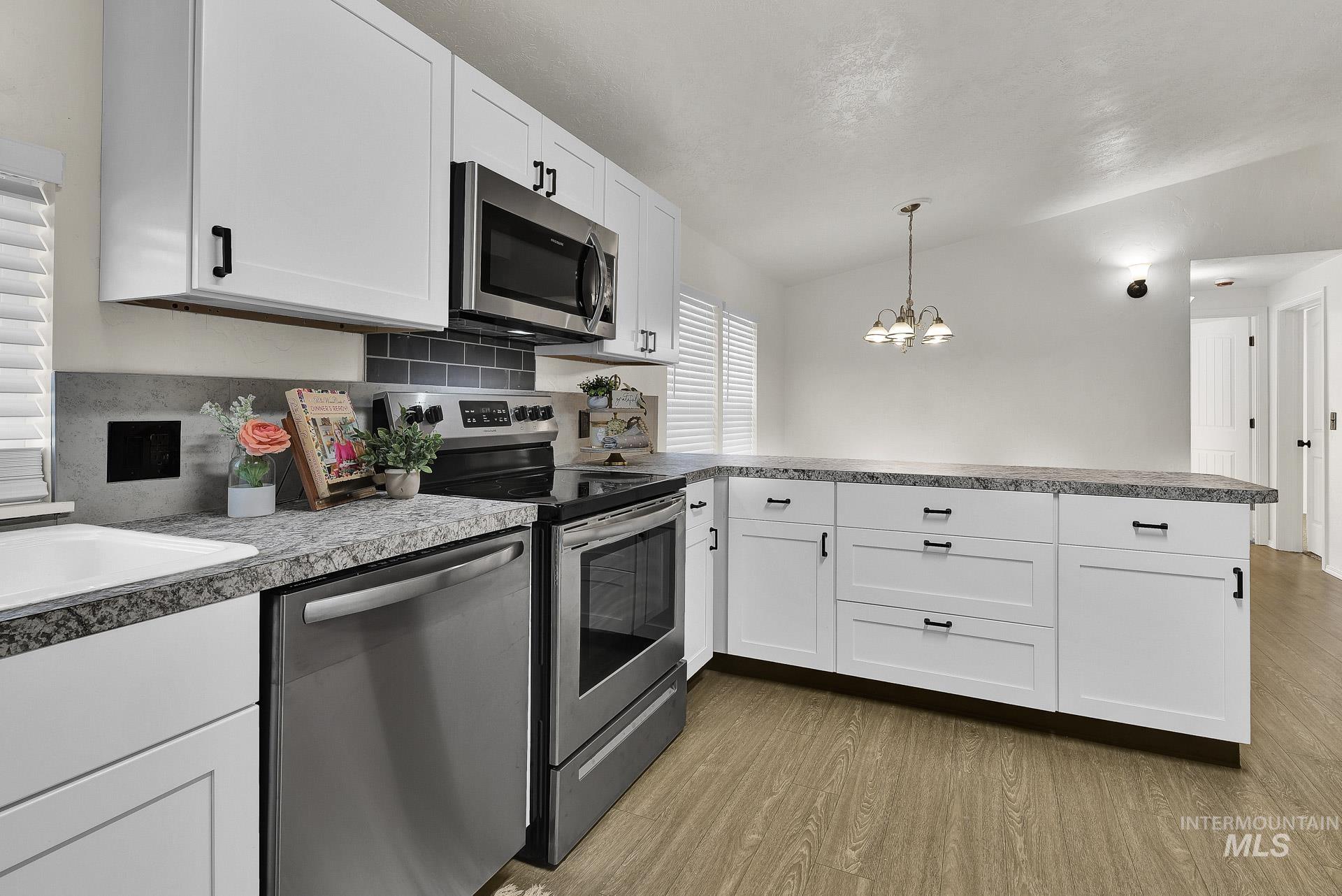 3249 Cherry Lane, Unit 23 Boise, ID 83705 - Photo 9 of 11 Kitchen with appliances with stainless steel finishes, vaulted ceiling, white cabinetry, light wood-type flooring, and a peninsula