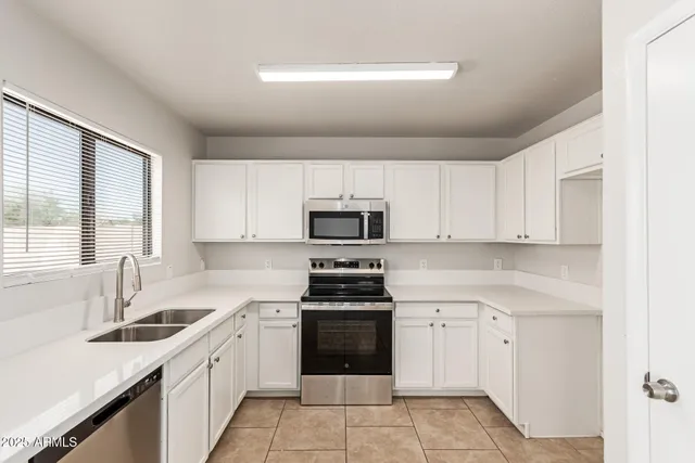 a kitchen with white cabinets appliances a sink and a window