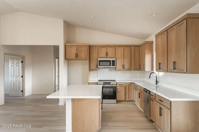 a kitchen with stainless steel appliances granite countertop a stove top oven a sink dishwasher and a refrigerator with wooden floor