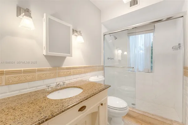 a bathroom with a granite countertop sink a toilet a mirror and shower